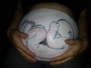 Vientre pintado en base blanco de con un bebe, haciendo efecto de la posicion que tiene actualmente dentro de la barriga de su mama